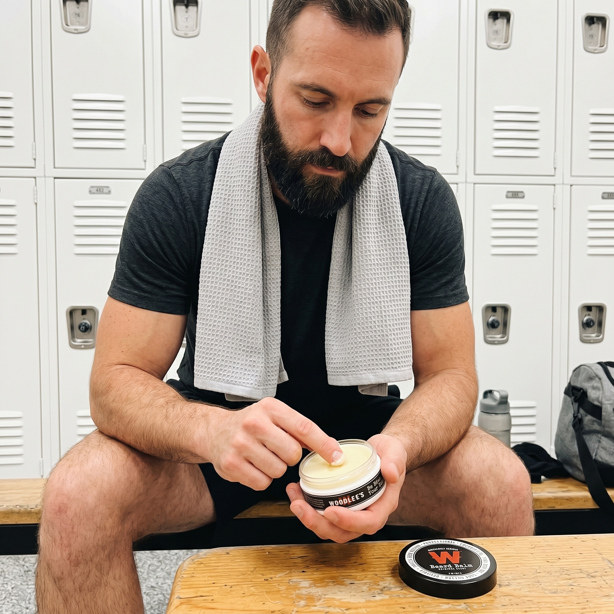 Man scooping a fingertip of Woodlee's Beard Balm in a gym locker room