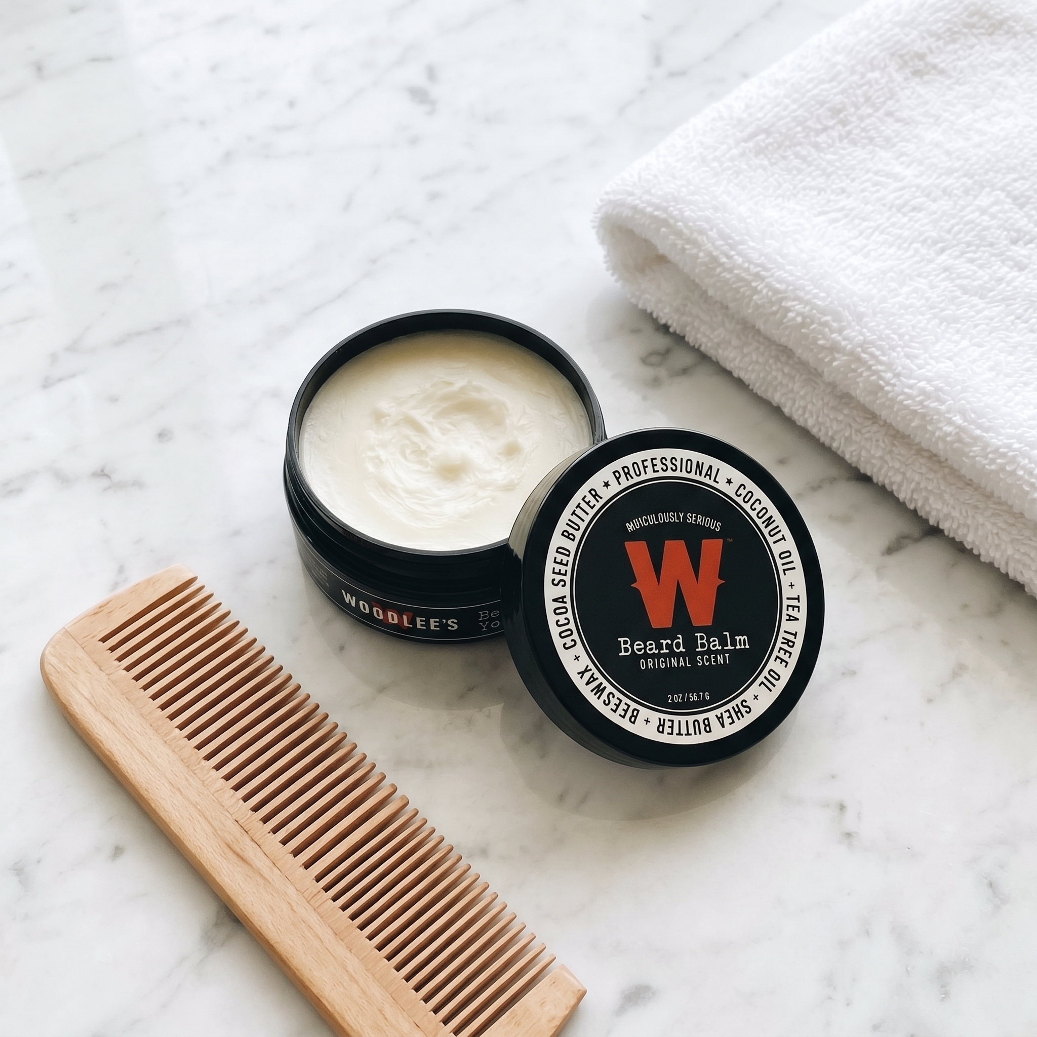 Open tin of Woodlee's Beard Balm on marble with a wooden comb and towel